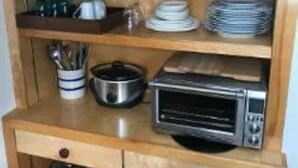 Uma cozinha compacta com micro-ondas, forno elétrico e prateleiras com louças e utensílios.