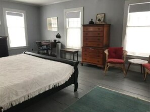 A bedroom with a bed, dresser, chair, desk, and windows.
