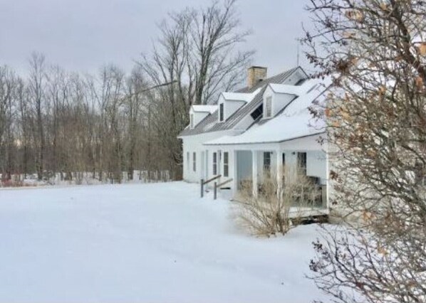 A snow-covered house with a symmetrical design, a chimney, and a porch.