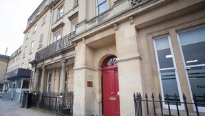 Un bâtiment historique avec une porte rouge, un balcon et une clôture en métal noir.