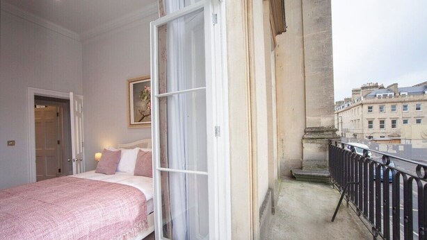 Une chambre avec un grand lit, une fenêtre et un balcon doté d’une balustrade.