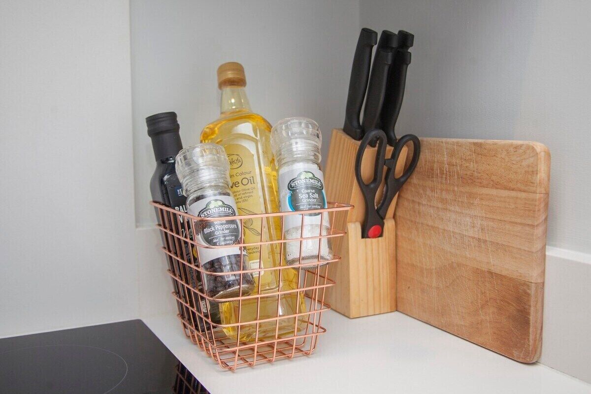 A kitchen counter with a copper spice rack holding various bottles, a wooden cutting board, and a pair of scissors.