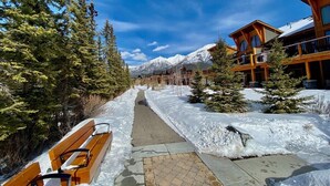 A snow-covered pathway leading to a lodge with wooden architecture and a mountain backdrop. - Spring Creek 3F 1600sf Corner 3BR/2BTH (Canmore)