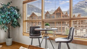 A room with a large window, two chairs, a small table with a plant, and a potted plant. - Spring Creek 3F 1600sf Corner 3BR/2BTH (Canmore)