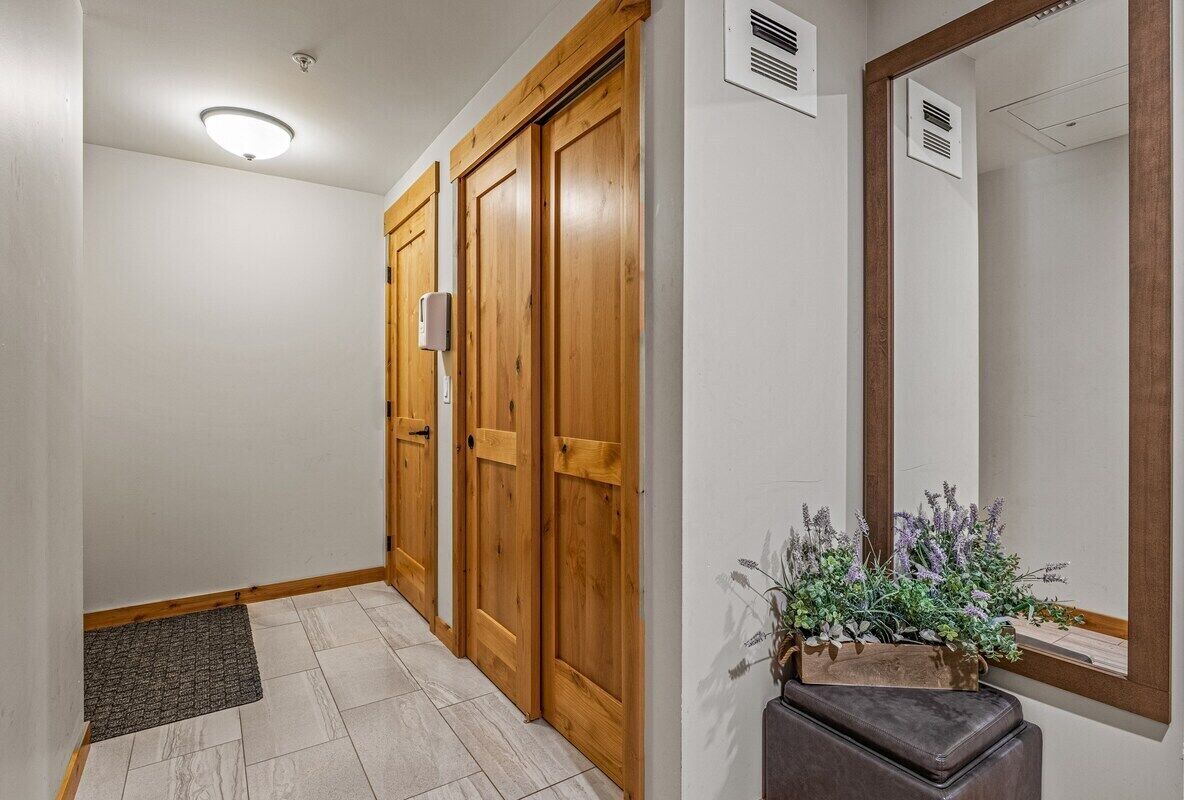 Un couloir avec des portes en bois, un petit tapis et une plante en pot.