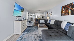A modern living room with a large flat-screen TV, a grey sectional sofa, and a patterned rug.