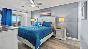 A bedroom with a bed, two bedside tables, a ceiling fan, and a view of the outside.
