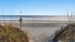 A beach path leading to the ocean with a signpost and sparse vegetation.