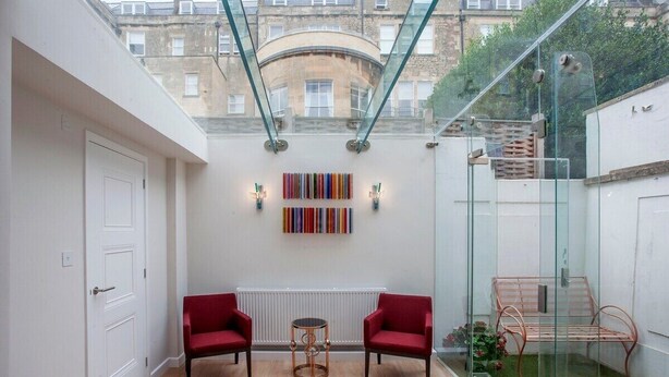 Un intérieur moderne avec un plafond en verre, deux fauteuils rouges, une petite table ronde et un banc en métal.