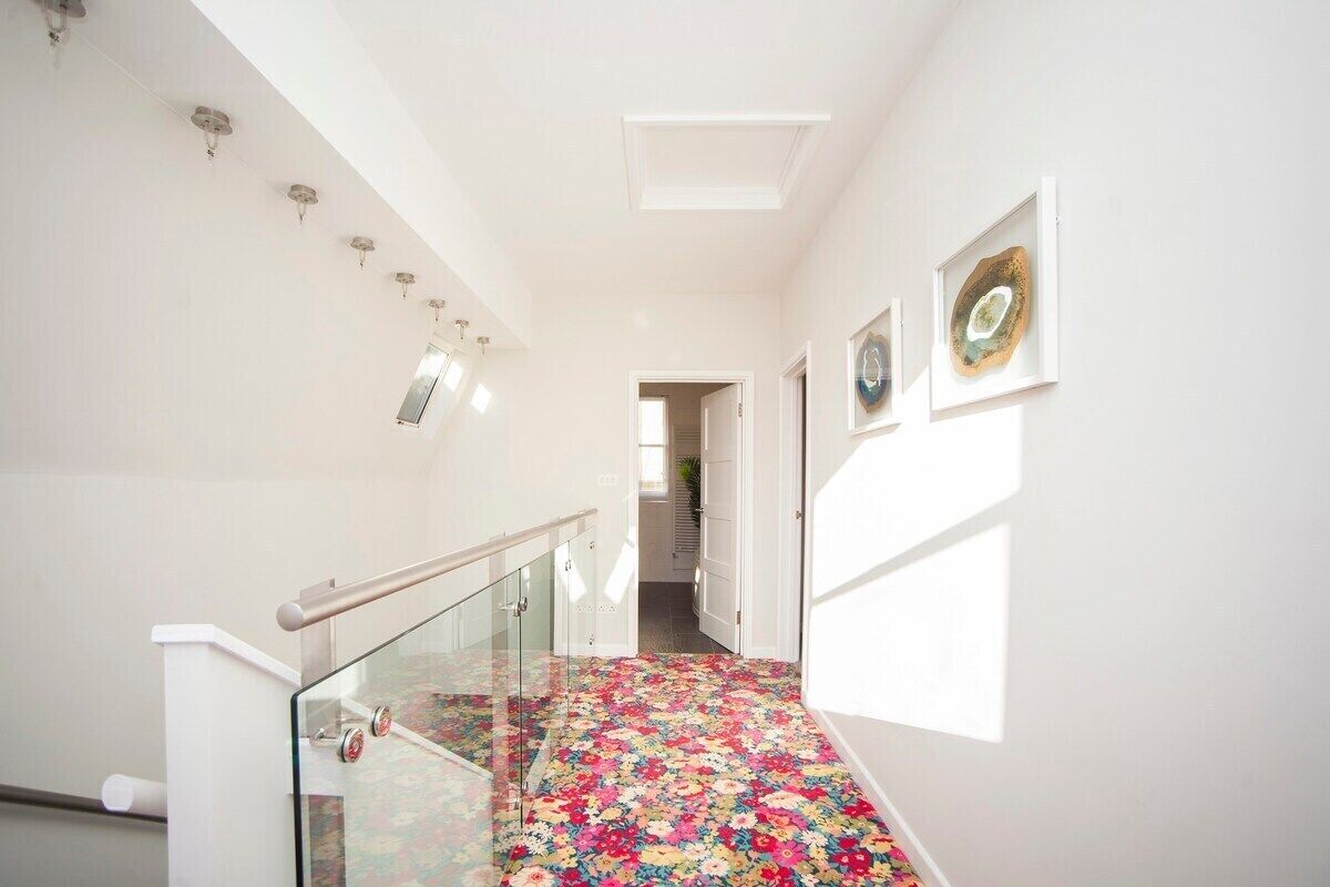 Un pasillo con barandilla de cristal, alfombra floral y cuadros en las paredes.