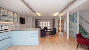 Une cuisine moderne dotée d’un îlot central, d’un coin repas avec une table en verre et d’un escalier avec une rampe en verre.