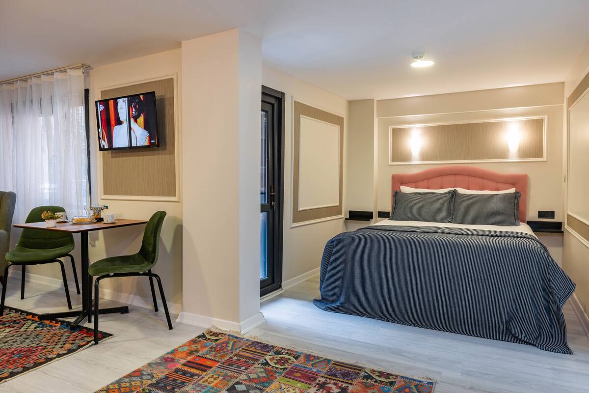 Una habitación de hotel moderna con una cama, un escritorio con sillas, un televisor y una alfombra estampada.