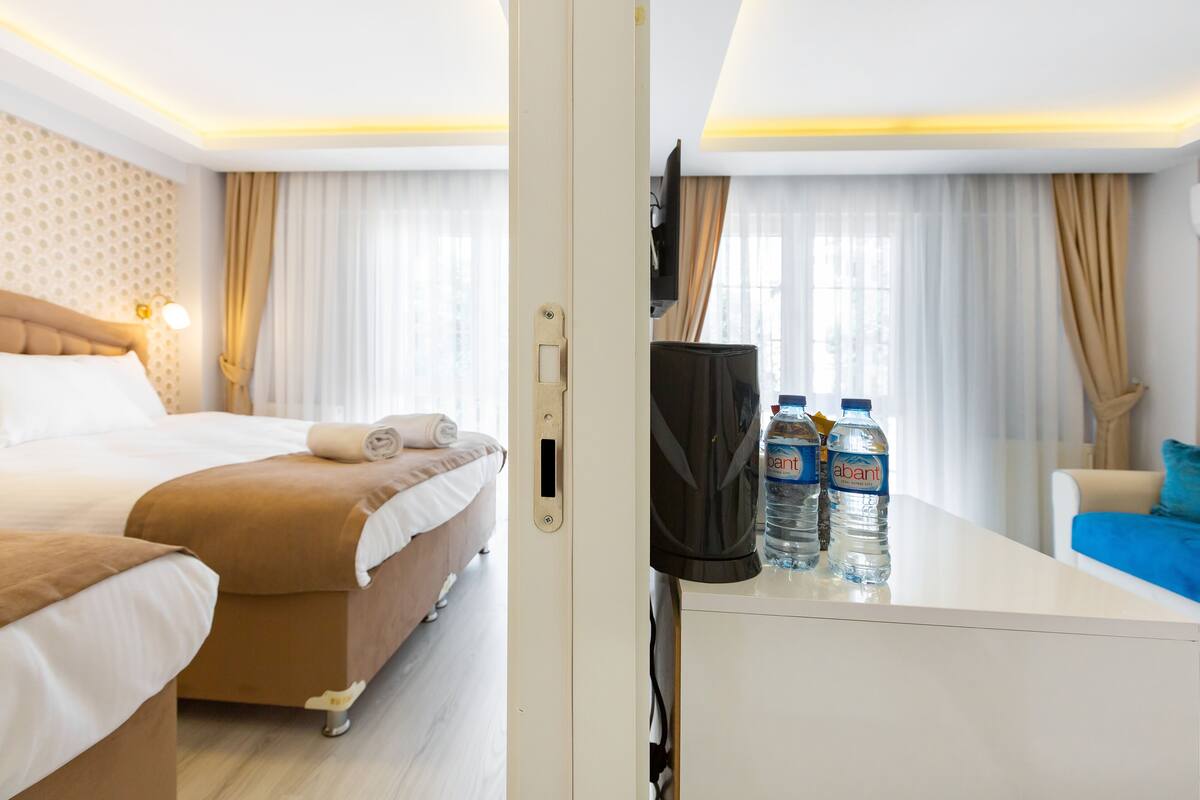 Una habitación de hotel con cama, escritorio con botellas de agua, televisor y ventana con cortinas.