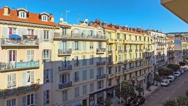 Una hilera de edificios de varios pisos con balcones, cielo despejado y automóviles estacionados a lo largo de la calle.