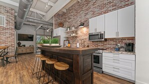 A kitchen with a brick wall, wooden bar stools, white cabinets, and stainless steel appliances. - The Bonnie (Bulverde)