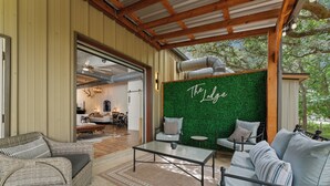 A cozy lounge area with wicker furniture, a glass coffee table, and a green wall with 'The Lodge' written on it. - The Bonnie (Bulverde)
