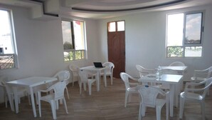 A room with white plastic tables and chairs, large windows, and a wooden door. - Hotel Daddy's (Thika)