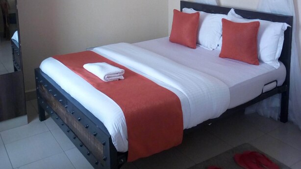 A neatly made bed with a red and white bedspread, two pillows, and a white towel on the side. - Hotel Daddy's (Thika)