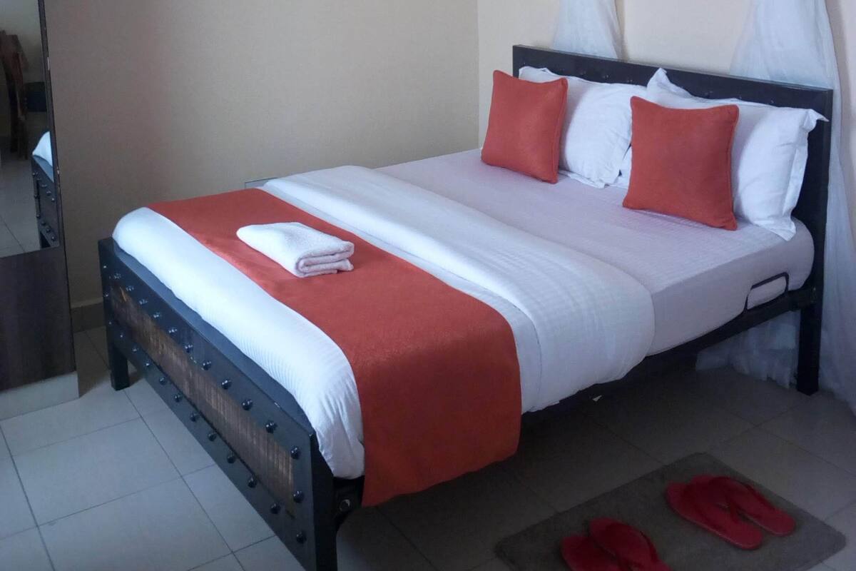 A neatly made bed with a red and white bedspread, two pillows, and a white towel on the side.