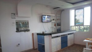 A kitchen with a counter, a television mounted above it, and a window with a view of trees. - Hotel Daddy's (Thika)