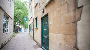 Un callejón estrecho con una puerta verde marcada con el número 24, junto a un edificio con una ventana y una puerta visibles.