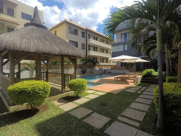 A pool area with a thatched gazebo, palm trees, and a well-maintained lawn.