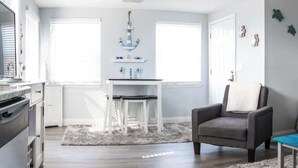 A modern kitchen with white cabinets, a grey chair, and a small table with a blue top. - Gulf Views Across The Street From Beach Access (Madeira Beach)