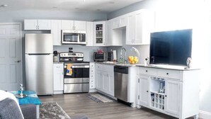 A modern kitchen with white cabinetry, stainless steel appliances, and a flat-screen TV. - Gulf Views Across The Street From Beach Access (Madeira Beach)
