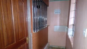 A narrow hallway with a wooden door on the left, a metal gate, and a tiled floor. A sign with the number 856479 is visible on the wall. - Ruby G Hotel and Club (Ruiru)