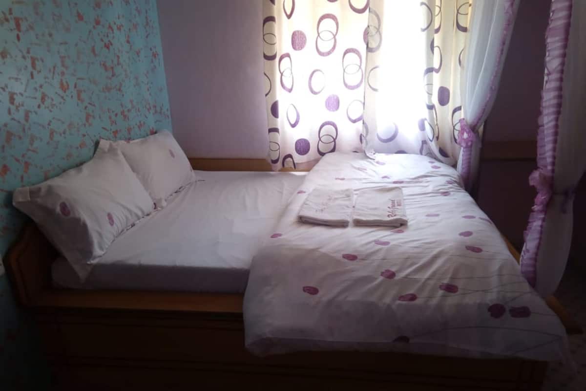 A single bed with a wooden frame, white bedding, and a floral-patterned pillow.