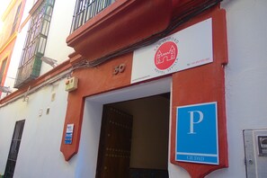 A building with a red facade, a sign for 'San Isidro Hostel Sevilla', and a blue parking sign. - San Isidoro Hostel Sevilla (Seville)