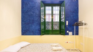 A room with a bed, a window with green shutters, a towel rack, and a wall-mounted phone. - San Isidoro Hostel Sevilla (Seville)