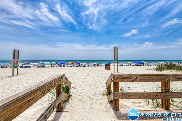 A beach with wooden railings, umbrellas, and a clear sky.