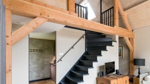 Un interior moderno con una escalera de madera, una zona de cocina y un espacio de sala con un sofá y una lámpara.