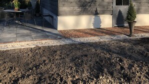 Una casa con techo de paja, un porche delantero y un pequeño jardín con mesa y sillas.