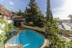 En swimmingpool omgivet af frodigt grønt og en lille bygning med et tagdækket tag.