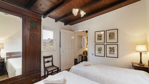 A hotel room with two beds, a wooden wardrobe, a chair, and framed pictures on the wall. - Quinta Florença - By Wehost (Funchal)