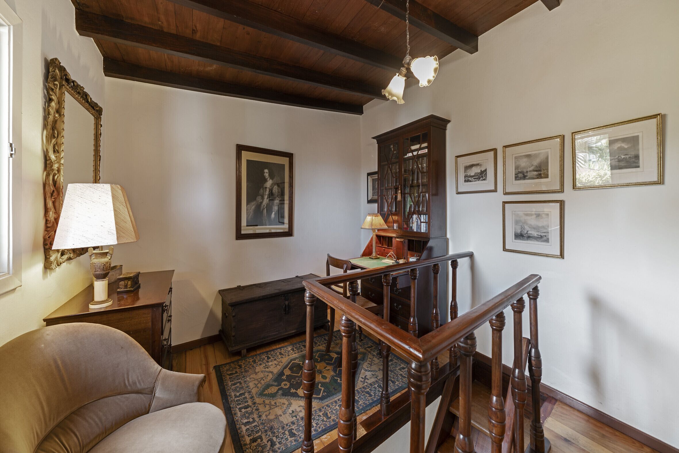 A room with a wooden staircase, a sofa, a lamp, a table, and framed pictures on the wall.