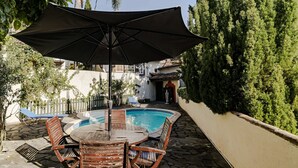 A poolside area with a table and chairs, a large umbrella, and a swimming pool. - Quinta Florença - By Wehost (Funchal)