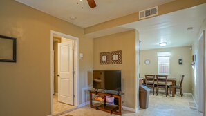 A living room with a TV on a wooden stand, a dining area with a table and chairs, and a hallway with a door leading to another room. - 2bd,1ba Remodeled Home w/large yard and Corn Hole Game (Los Ranchos De Albuquerque)