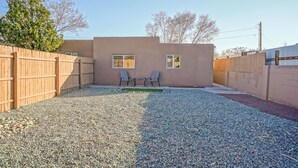 A backyard with a wooden fence, two windows, and a gravel patio. - 2bd,1ba Remodeled Home w/large yard and Corn Hole Game (Los Ranchos De Albuquerque)
