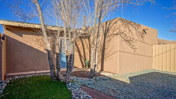 A courtyard with a brown building, a tree-lined pathway, and a small lawn area. - 2bd,1ba Remodeled Home w/large yard and Corn Hole Game (Los Ranchos De Albuquerque)