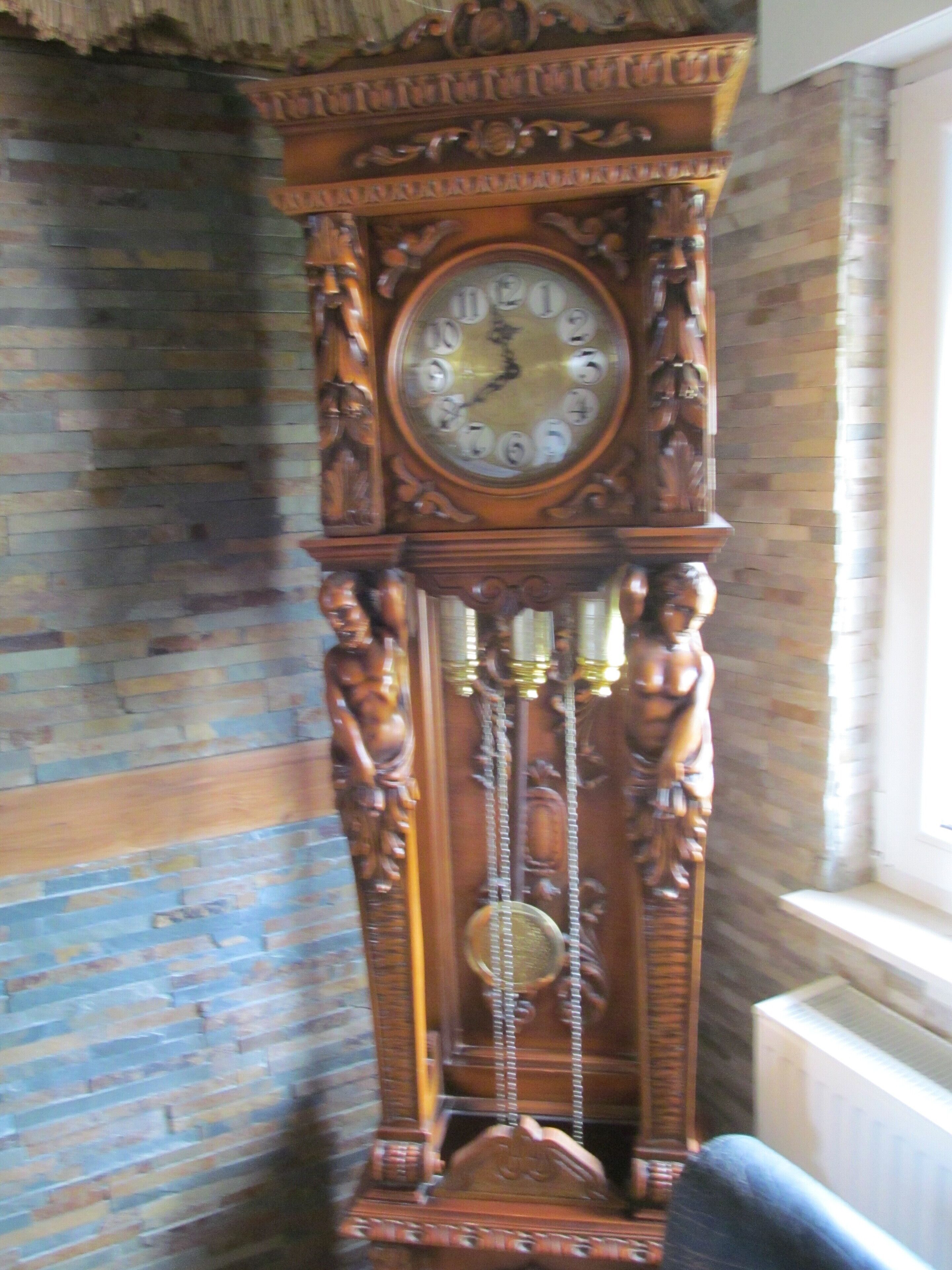 Une grande horloge comtoise en bois, richement décorée de sculptures complexes et dotée de plusieurs pendules.