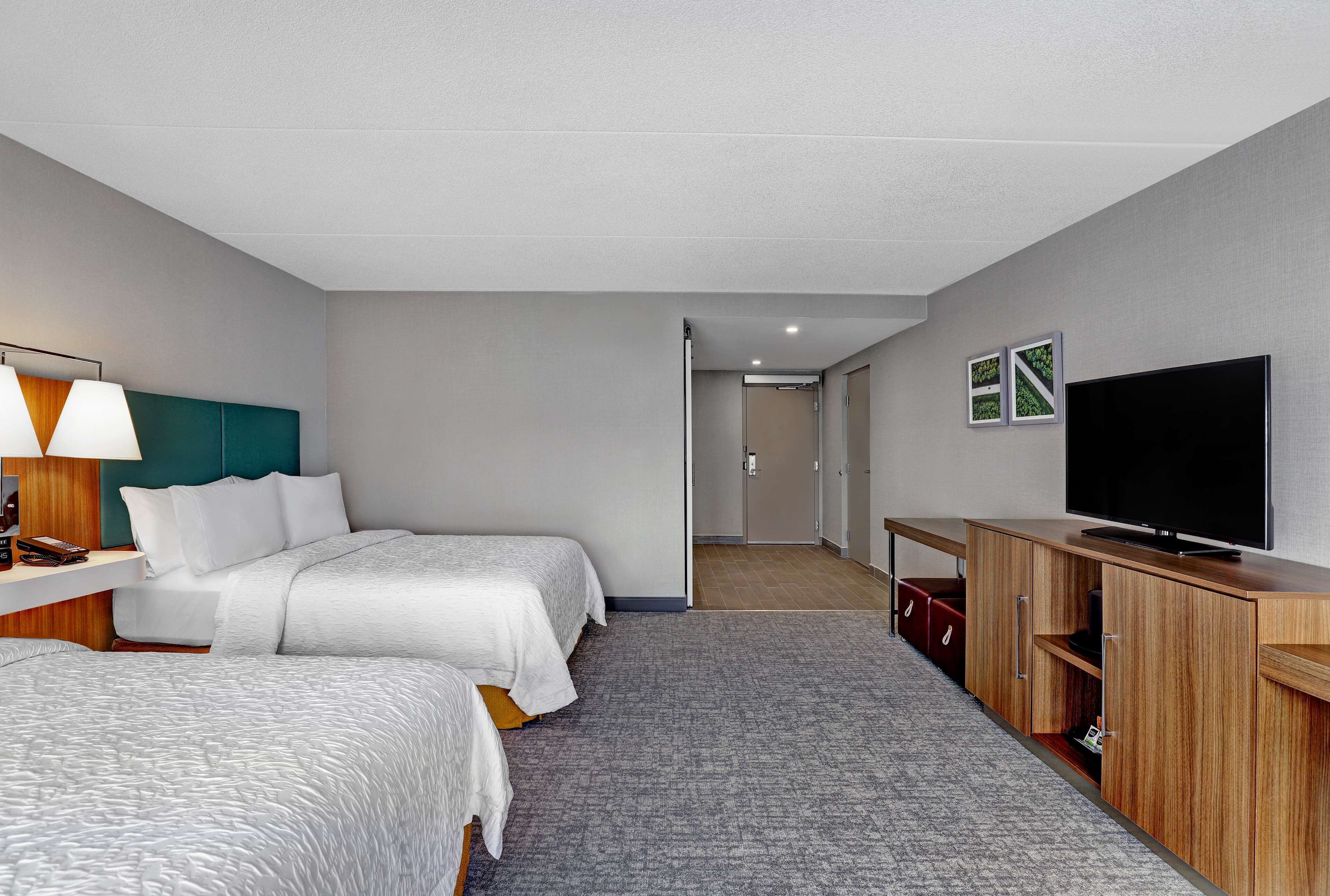 Une chambre d’hôtel avec deux lits, une télévision, un bureau avec une lampe et une armoire.