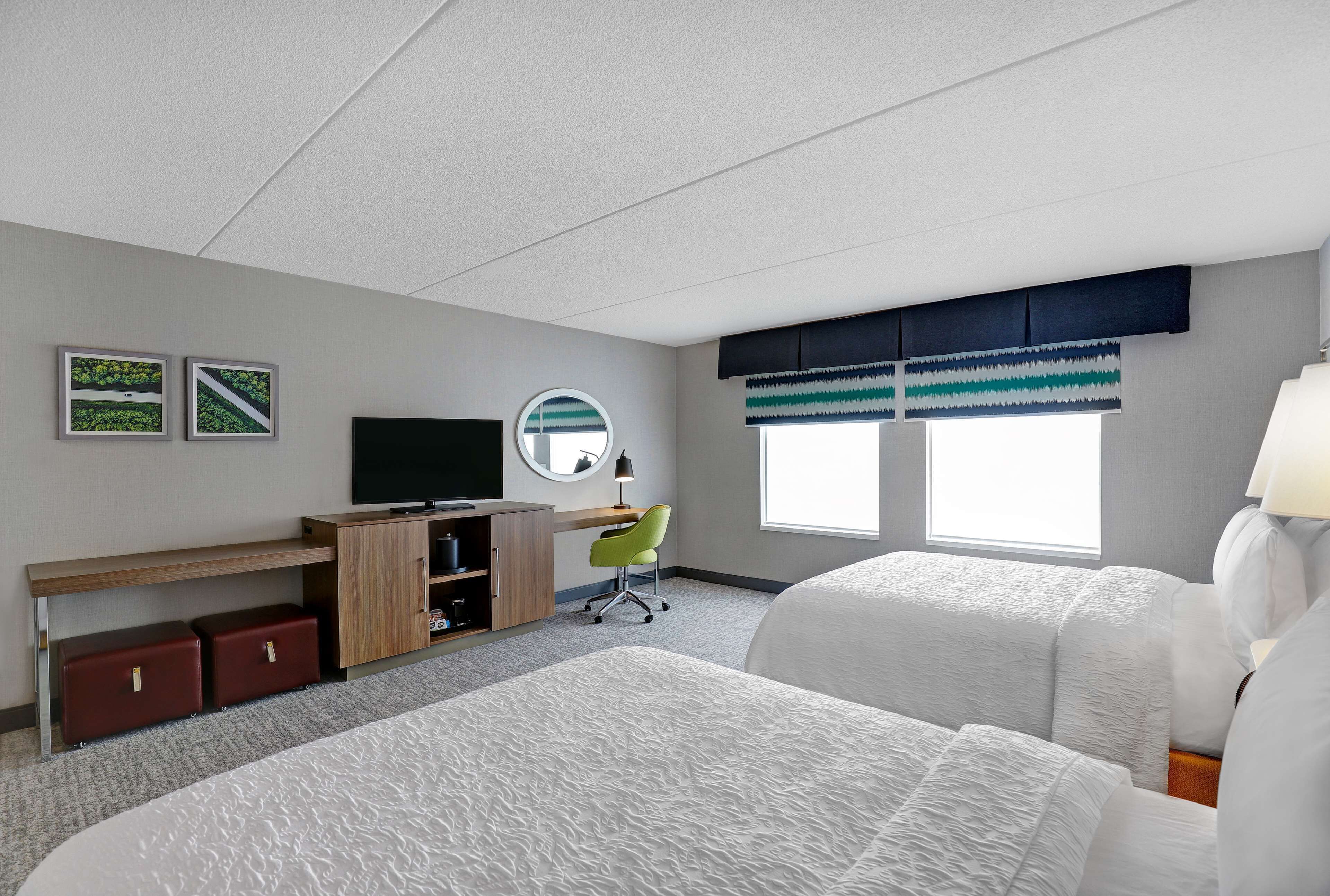 A hotel room with two beds, a desk, a chair, a television, and a window with blinds.