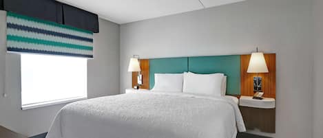 Habitación de hotel con una cama grande, dos mesitas de noche con lámparas, una ventana con persiana a rayas y un cabecero color aguamarina.
