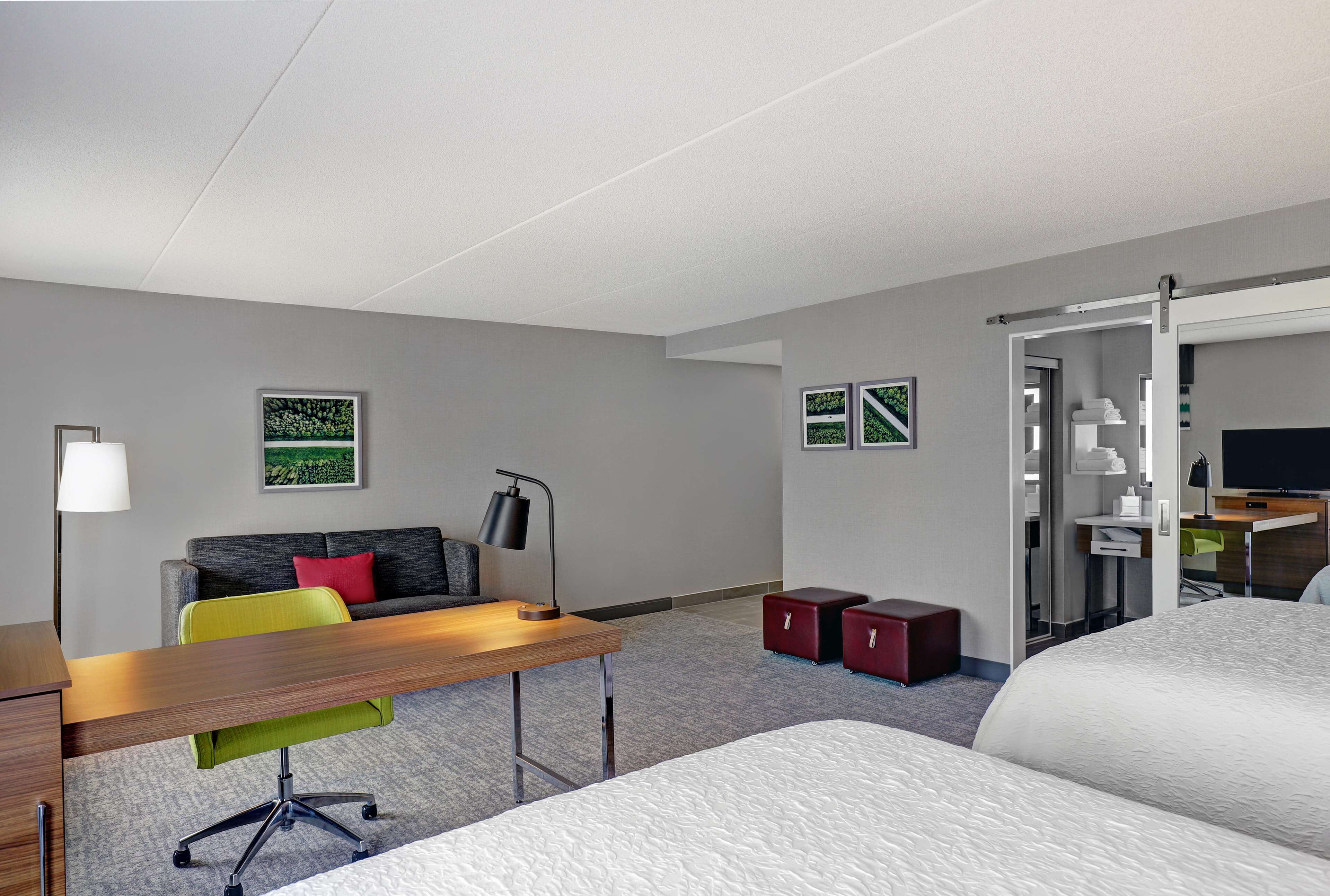 Habitación de hotel con cama, escritorio con silla, sofá, dos cajas rojas para guardar objetos y televisión.