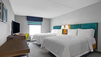 A hotel room with two beds, a desk, a television, and a window with blinds.