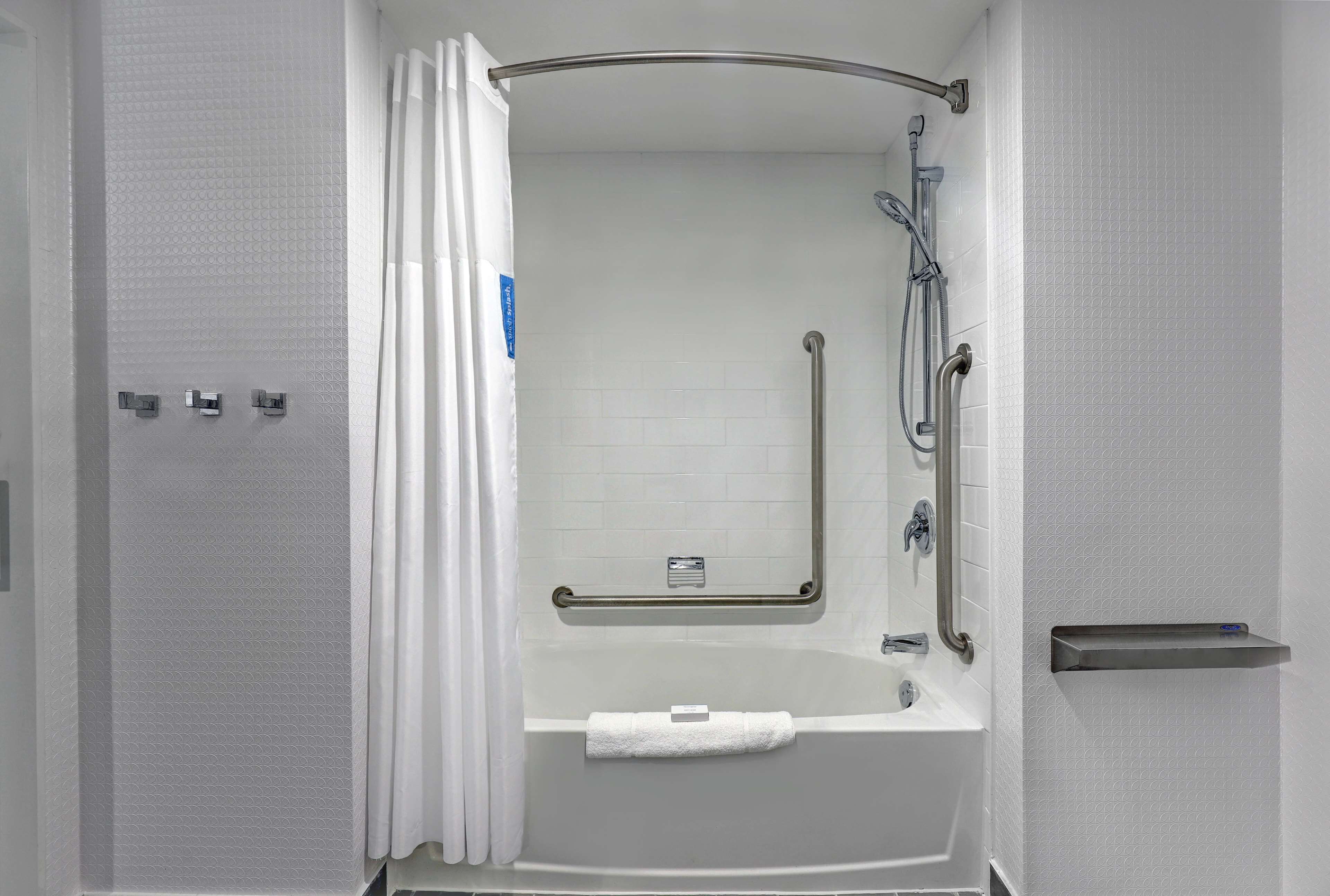 A modern bathroom with a walk-in shower, grab bars, a towel rack, and a shelf.