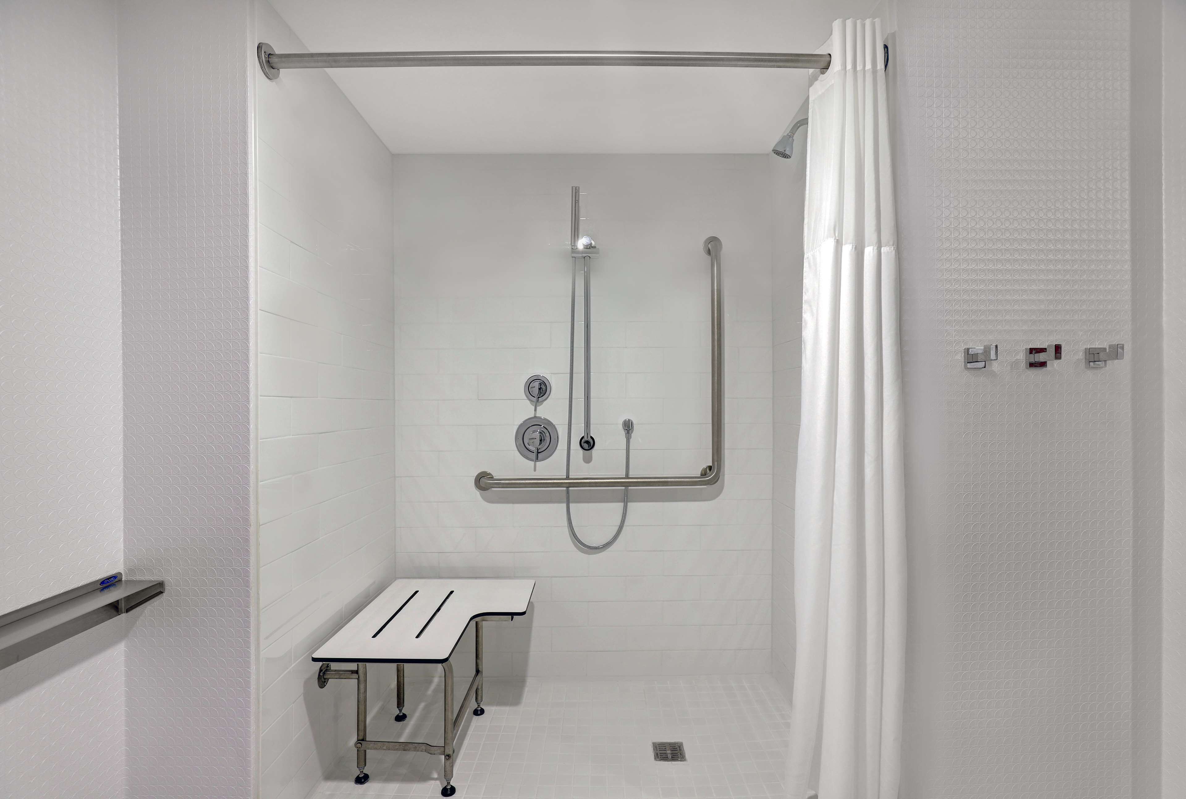 A shower area with a glass door, a handheld showerhead, a wall-mounted faucet, and a small table with a tray.